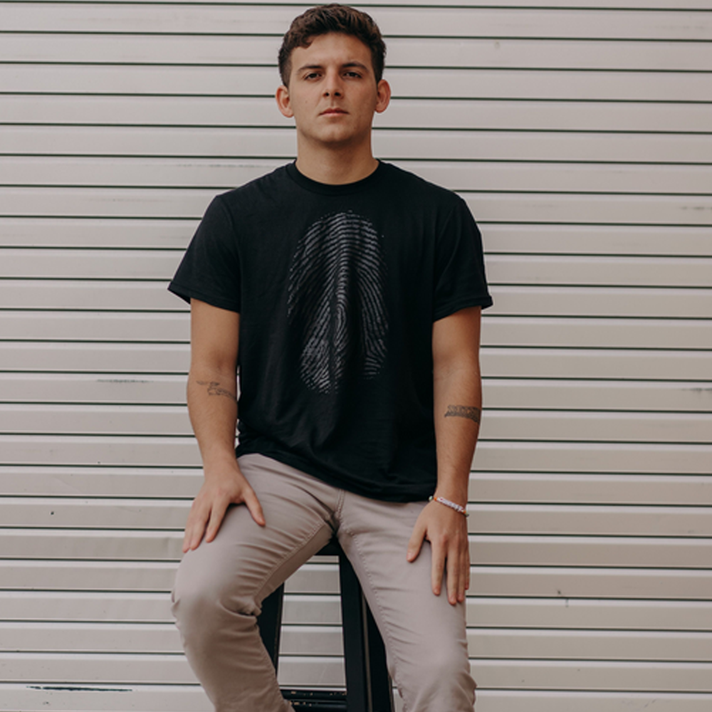 Front view of a man in a black shirt displaying a bold thumbprint design that symbolizes the message: 'God has given you a unique fingerprint.