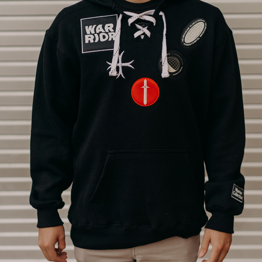A hoodie with a hockey fit, featuring 'Warrior' on the right shoulder, three patches on the left, and a chunky neck drawstring.